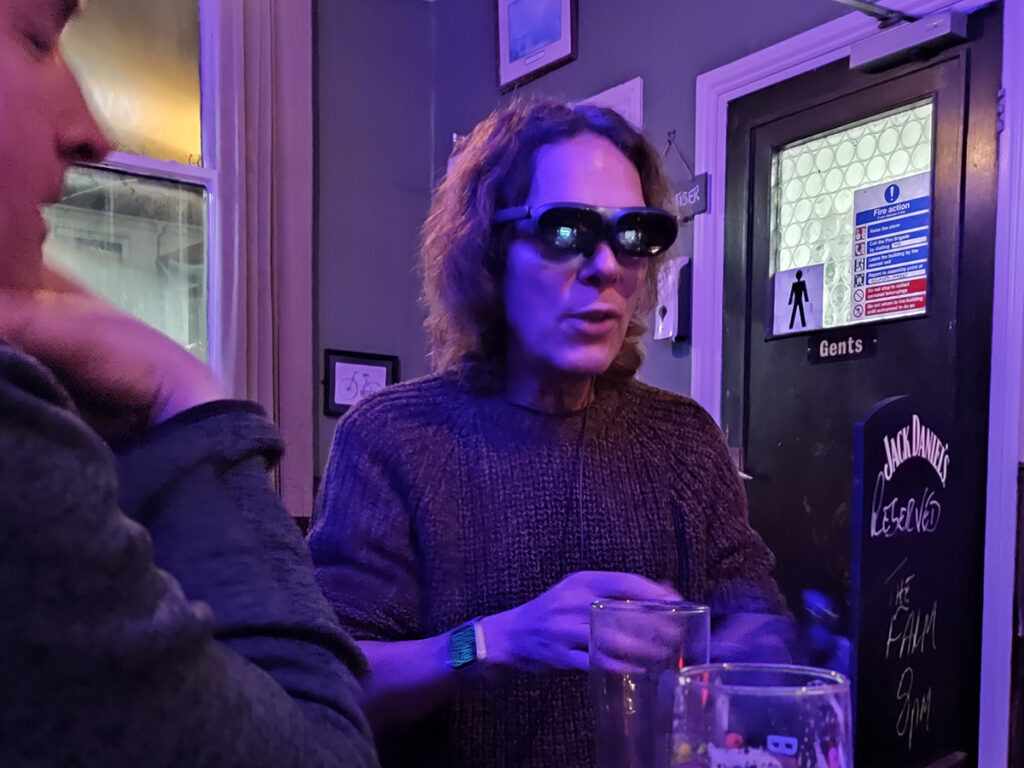 A man with long hair uses AR glasses connected to a phone
